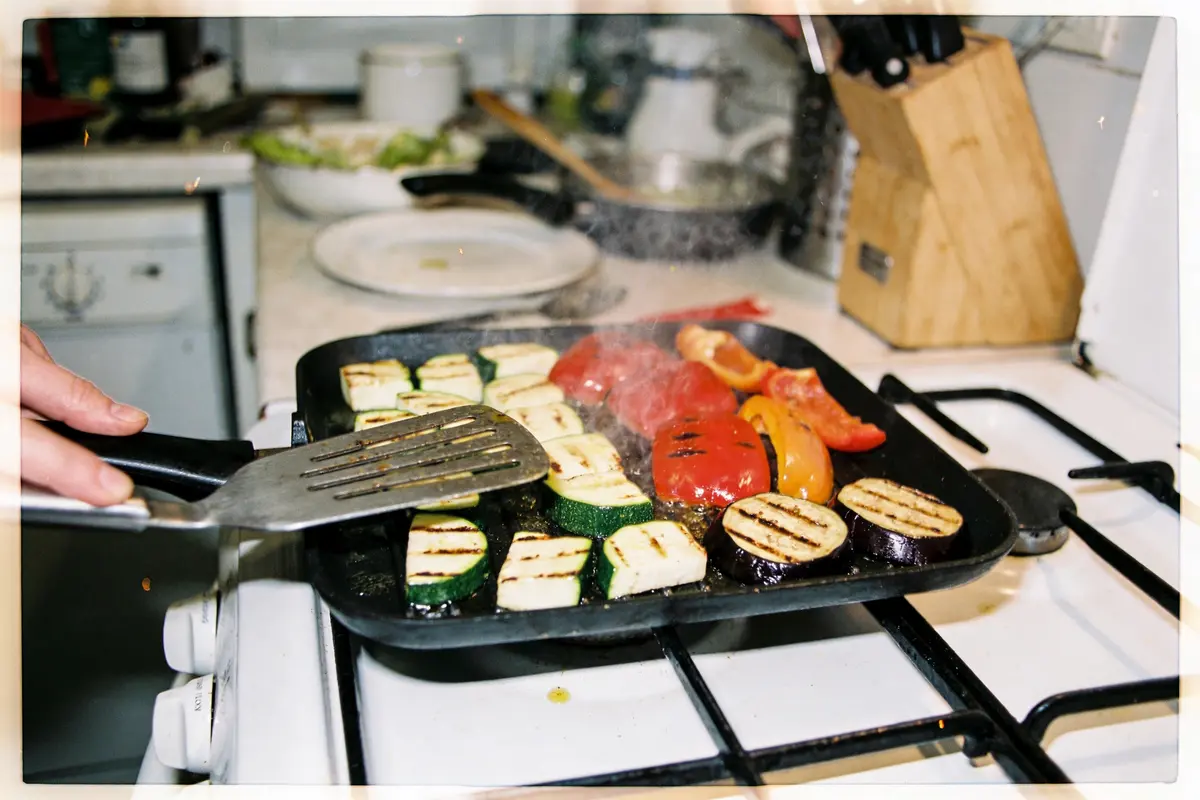 Légumes grillés sur poêle avec spatule, cuisine en arrière-plan, cuisson sur gazinière.
