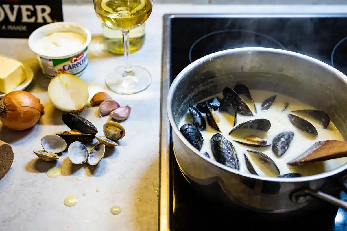 Casserole de moules à la crème sur cuisinière, avec ingrédients comme oignon, ail, beurre et vin blanc.