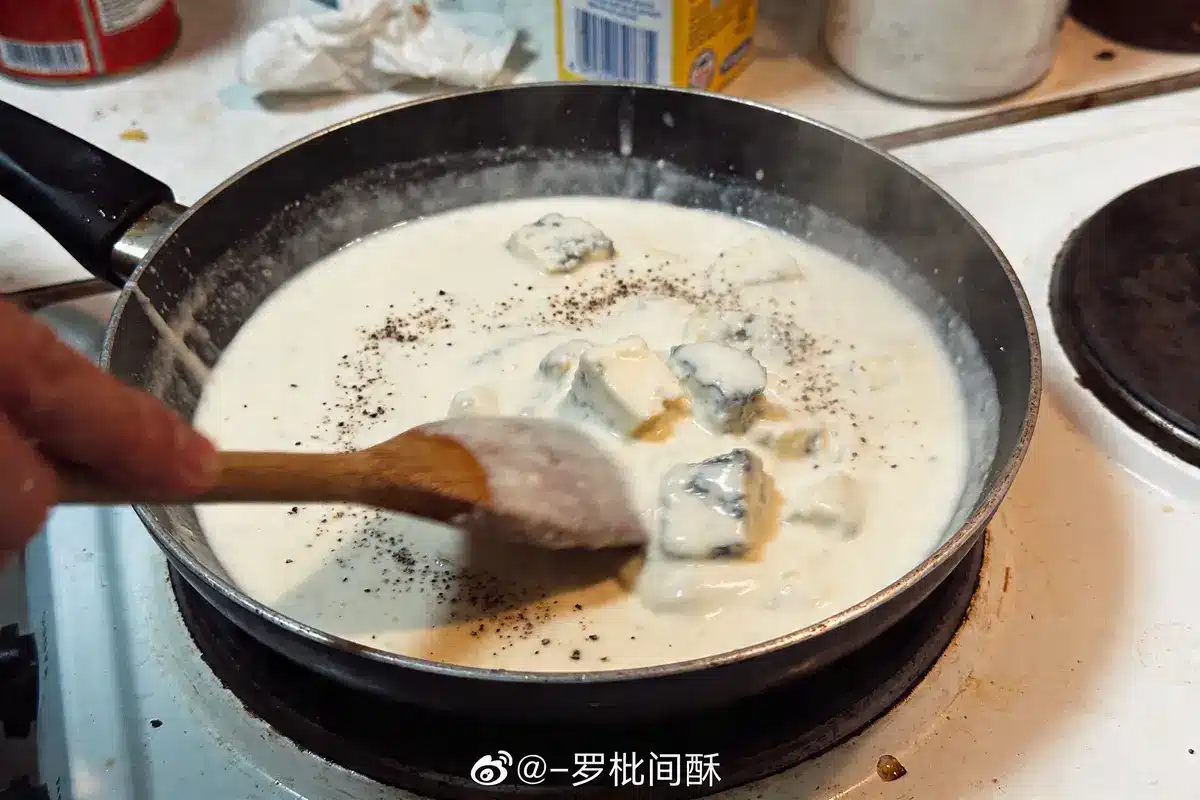 Poêle avec sauce crémeuse, fromage bleu, poivre, cuillère en bois. Cuisine en cours sur la cuisinière.