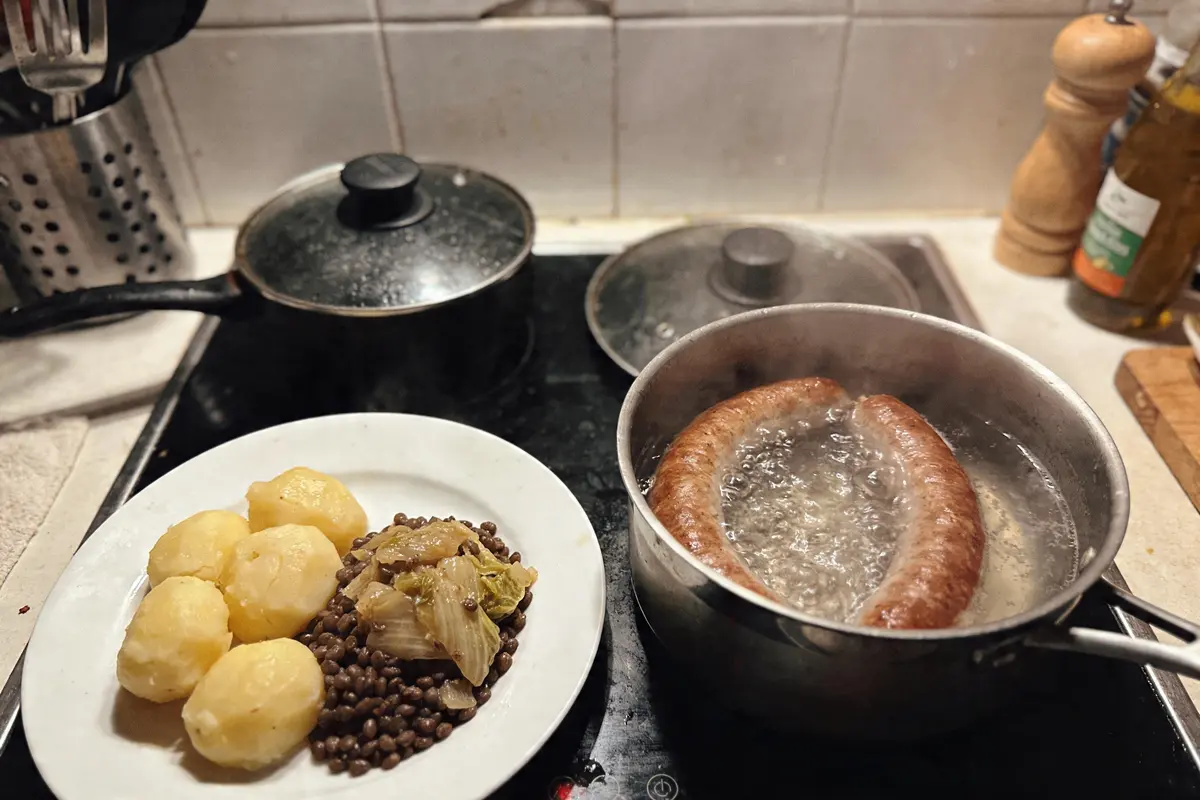 Assiette de pommes de terre, lentilles et choux cuits, avec saucisses bouillonnant dans une casserole.
