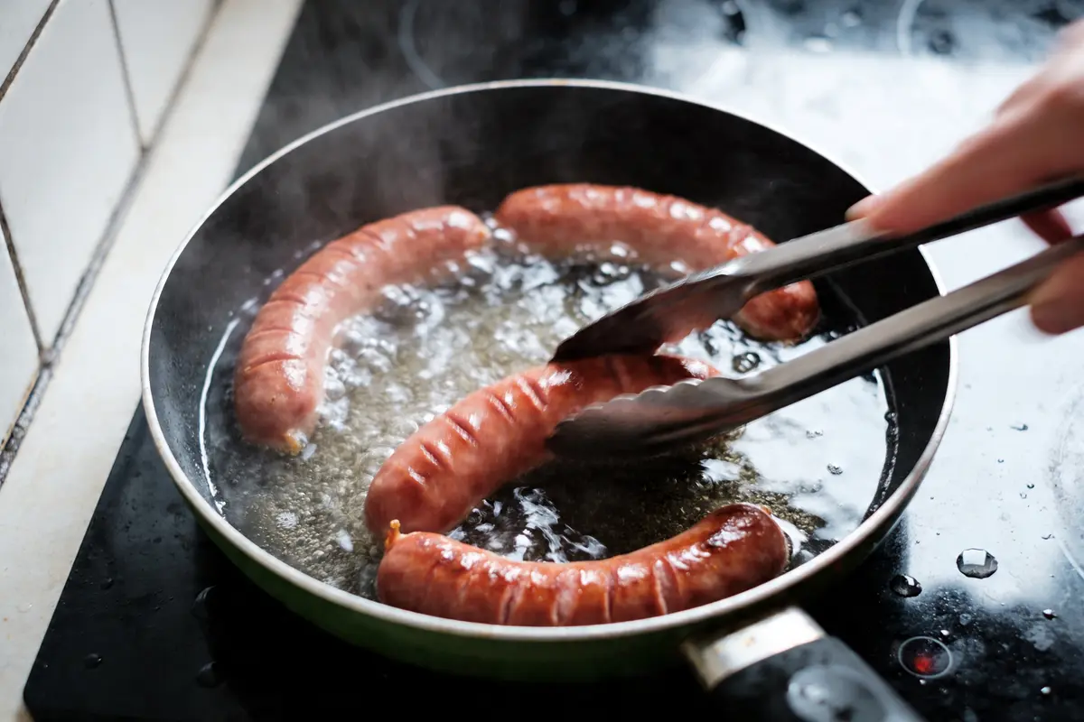 Saucisses brunes cuisant dans une poêle sur la cuisinière, saisies à la pince.