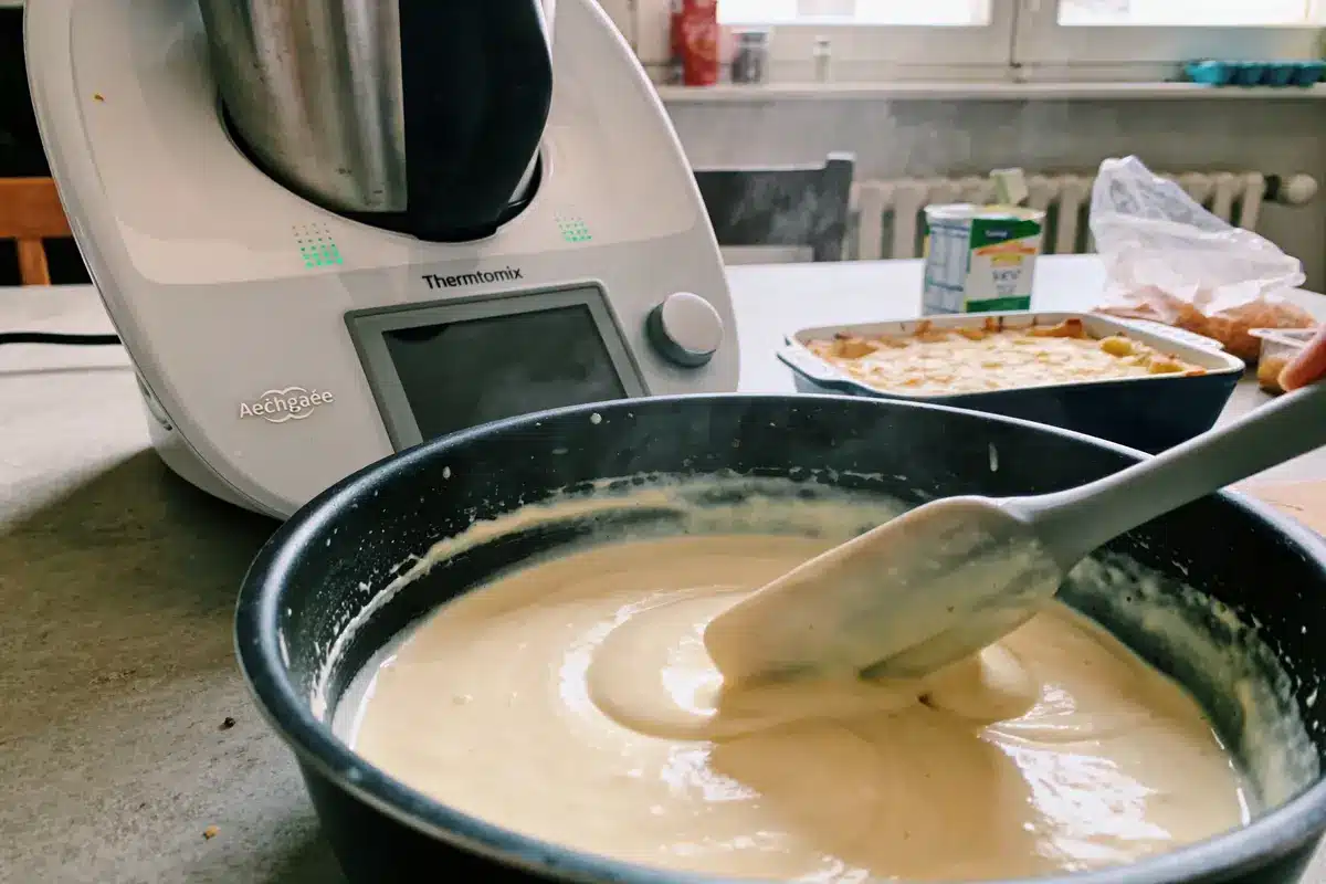 Bol de pâte mélangée à la spatule devant un robot culinaire sur plan de travail cuisine.