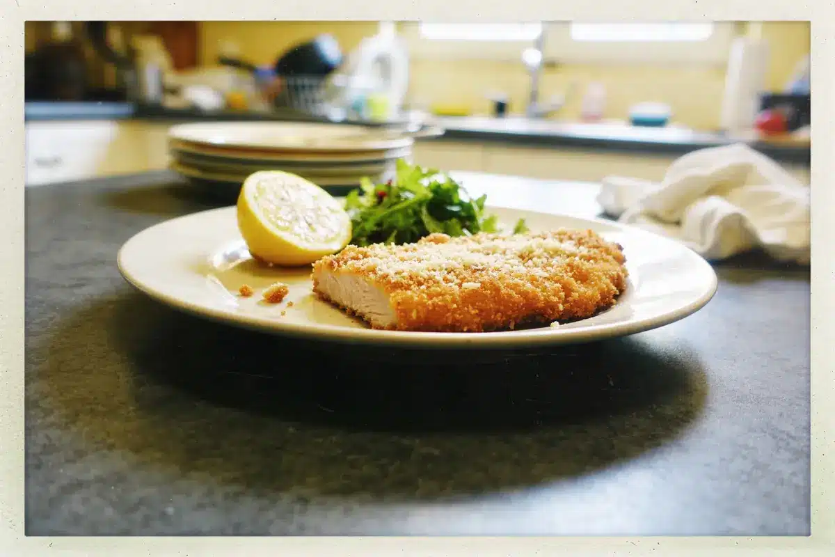 Assiette de poulet pané, demi-citron, salade verte, fond flou cuisine.