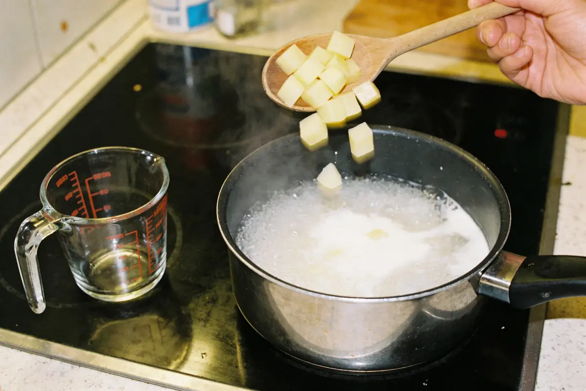 Une cuillère ajoute des cubes de pomme de terre à l'eau bouillante dans une casserole.