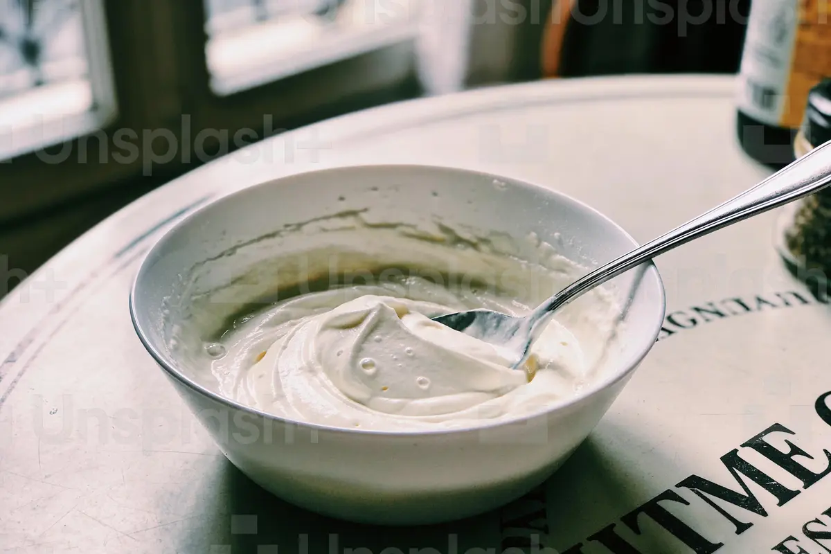 Bol de crème épaisse avec cuillère sur table blanche, près de la fenêtre.