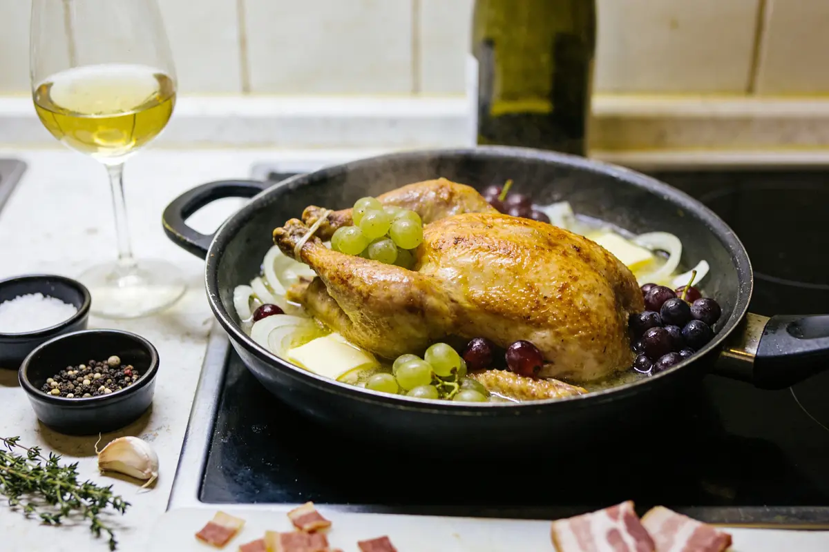 Poulet rôti avec raisins dans poêle, verre de vin blanc et ingrédients.
