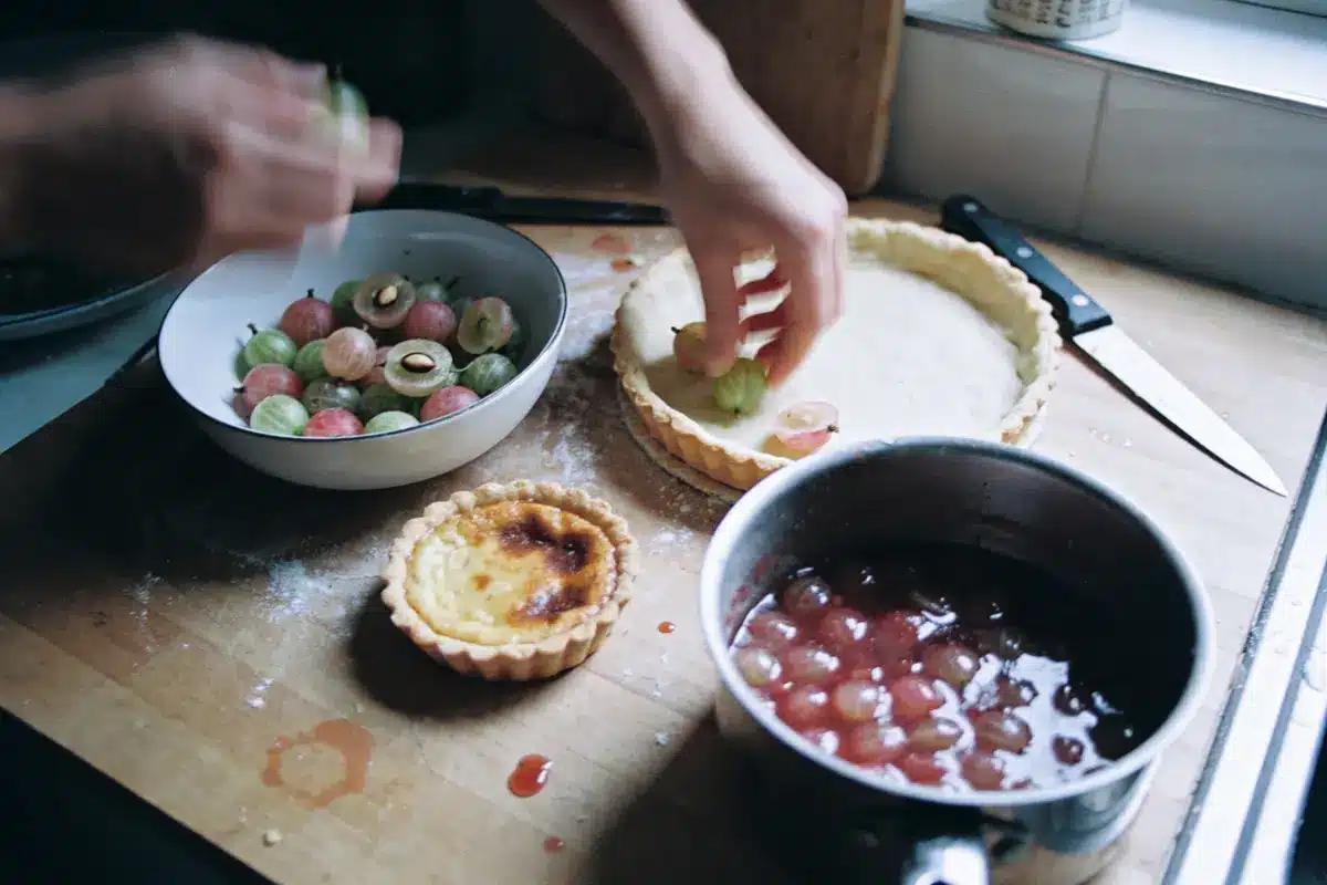 Des mains préparant une tarte aux groseilles avec pâte, fruits, couteau et casserole.