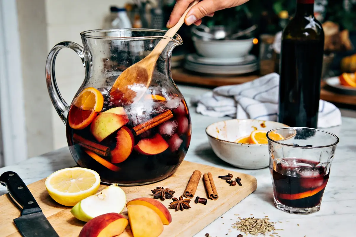 Pichet de sangria avec fruits, épices et verre sur table. Main mélangeant avec cuillère en bois.