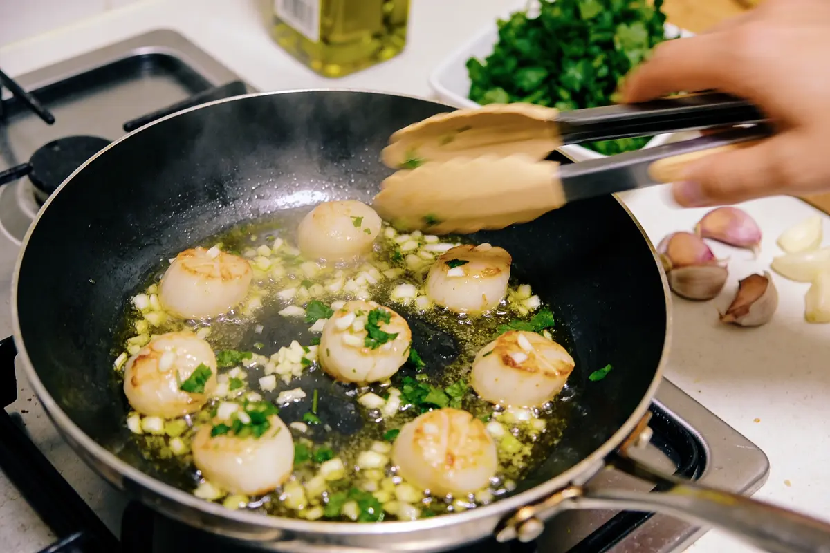 Noix de Saint-Jacques poêlées avec ail et persil dans une poêle sur la cuisinière.