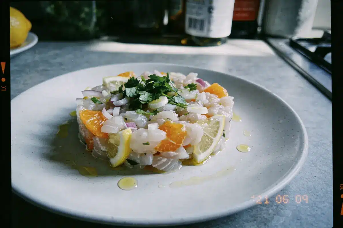 Tartare de poisson avec agrumes, herbes fraîches, huile d'olive, présenté sur assiette blanche dans cuisine.
